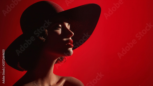 Elegant woman in a wide-brimmed hat with bold red lips against a red background