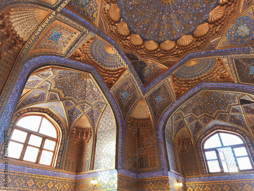 Ornate interior of Ak Saray Mausoleum in Samarkand featuring golden muqarnas and blue tilework. Ideal for travel publications, cultural heritage materials, and architectural studies.