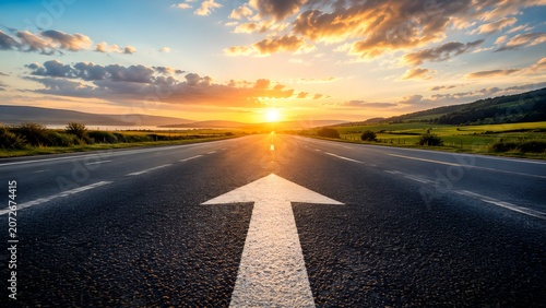 White directional arrow painted on asphalt highway leading to sunset. Concept of strategic business vision, future journey, and logistics supply chain.