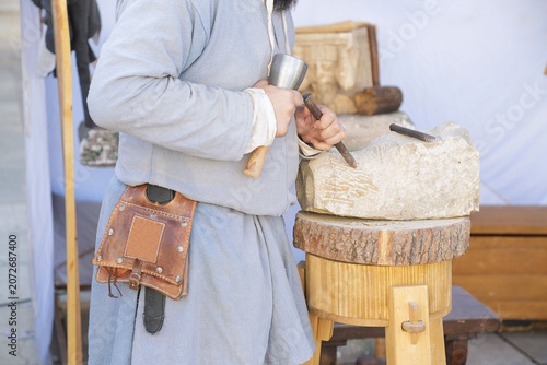 Artisan carving a stone block with a mallet and chisel in a traditional stone‑carving workshop.