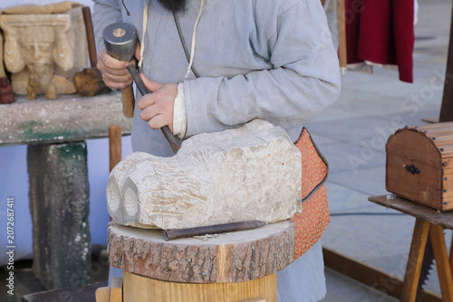 Artisan carving a stone block with a mallet and chisel in a traditional stone‑carving workshop.