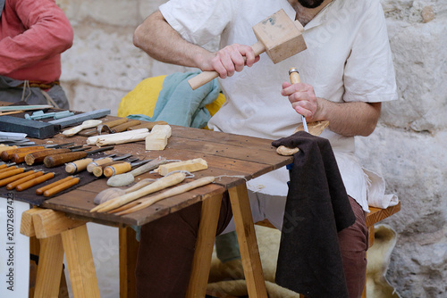 Artisan carving wood with a mallet and chisel at a traditional woodworking bench.