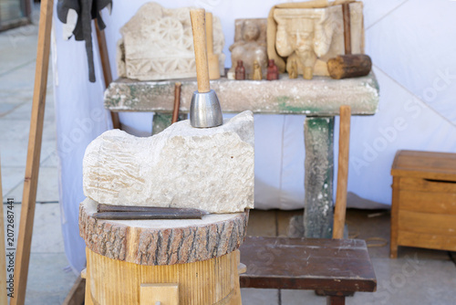 Stone carving workspace with a mallet, chisel, and a partially carved stone block in an artisan workshop.