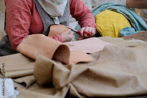 Artisan cutting leather or thick fabric with scissors at a traditional craft workshop.