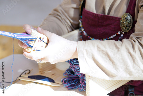 Artisan weaving colorful yarn on a small handheld loom during traditional textile work.