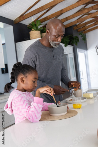 African American man and child in pink hoodie making breakfast at kitchen island with croissant