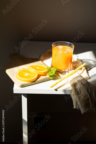 Fresh orange juice in glasses with ice cubes and mint in harsh sunlight. A high-angle studio shot of two glasses filled with vibrant orange juice or citrus smoothie. The scene is illuminated by harsh,
