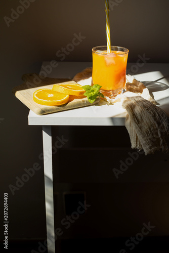 Fresh orange juice in glasses with ice cubes and mint in harsh sunlight. A high-angle studio shot of two glasses filled with vibrant orange juice or citrus smoothie. The scene is illuminated by harsh,