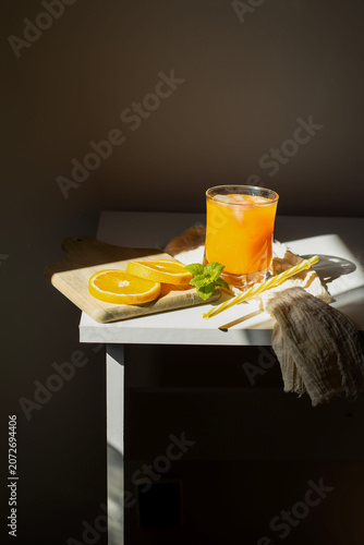 Fresh orange juice in glasses with ice cubes and mint in harsh sunlight. A high-angle studio shot of two glasses filled with vibrant orange juice or citrus smoothie. The scene is illuminated by harsh,