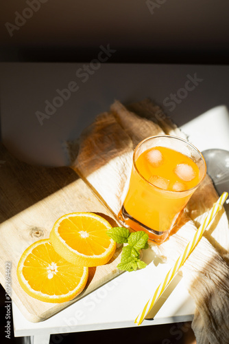 Fresh orange juice in glasses with ice cubes and mint in harsh sunlight. A high-angle studio shot of two glasses filled with vibrant orange juice or citrus smoothie. The scene is illuminated by harsh,