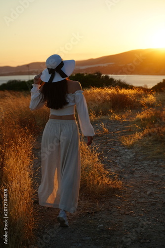 Woman Walking Through Golden Field At Sunset