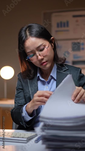 Stressed asian businesswoman sorting through paperwork at night