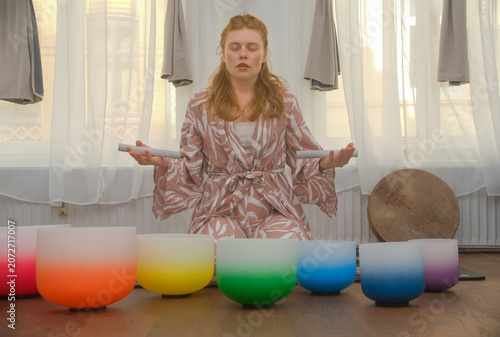 Young redhead woman in meditation with crystal singing bowls, immersed in sound, vibration and mindfulness during a relaxing wellness session