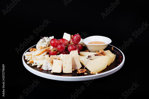Premium cheese platter with grapes walnuts and honey on isolated black background