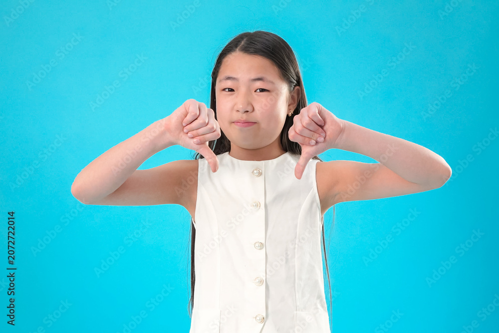 Wall Mural Disappointed young girl with thumbs down gesture showing her disapproval and sad
