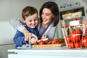 Mother teaching son to cut tomato on cutting board at kitchen