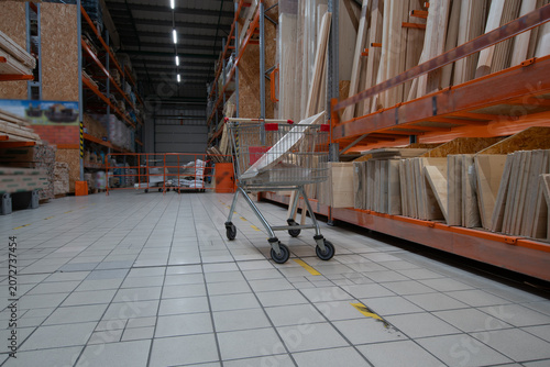 Empty shopping cart in a large hardware store aisle with shelves full of building materials