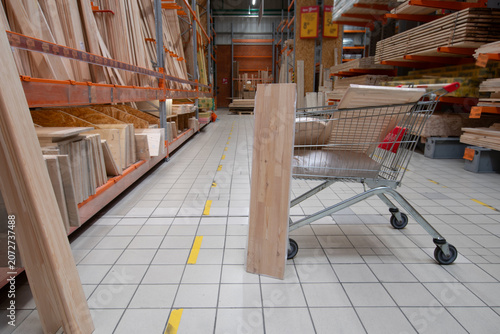 Shopping cart in a store aisle with wooden boards and supplies near the construction area around noon