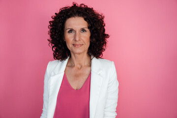 Mature businesswoman wearing white blazer on pink background