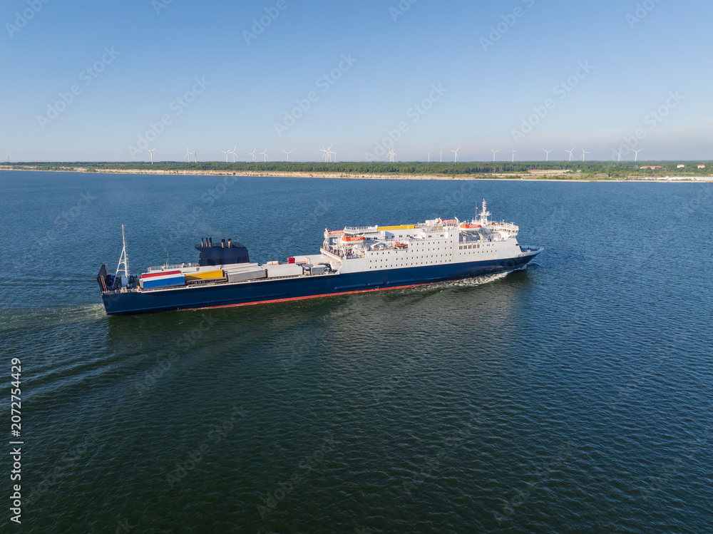 Fototapeta premium Aerial drone view of a Ro-Pax cargo passenger ferry ship sailing in the Baltic Sea near a coastline with wind turbines