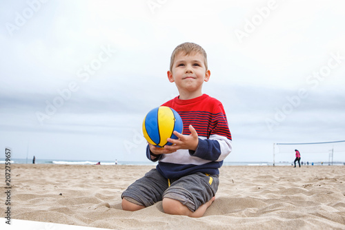 Young Boy Playing With a Colorful Beach Ball on a Sandy Shoreline During a Cloudy Afternoon