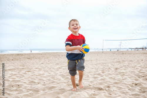 Young Boy Playing With a Colorful Beach Ball on a Sandy Shoreline During a Cloudy Afternoon