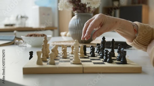 Side view closeup shot of senior woman and senior man playing chess in retirement home, moving wooden pieces on board. Clip for promoting active aging, cognitive health and senior care services