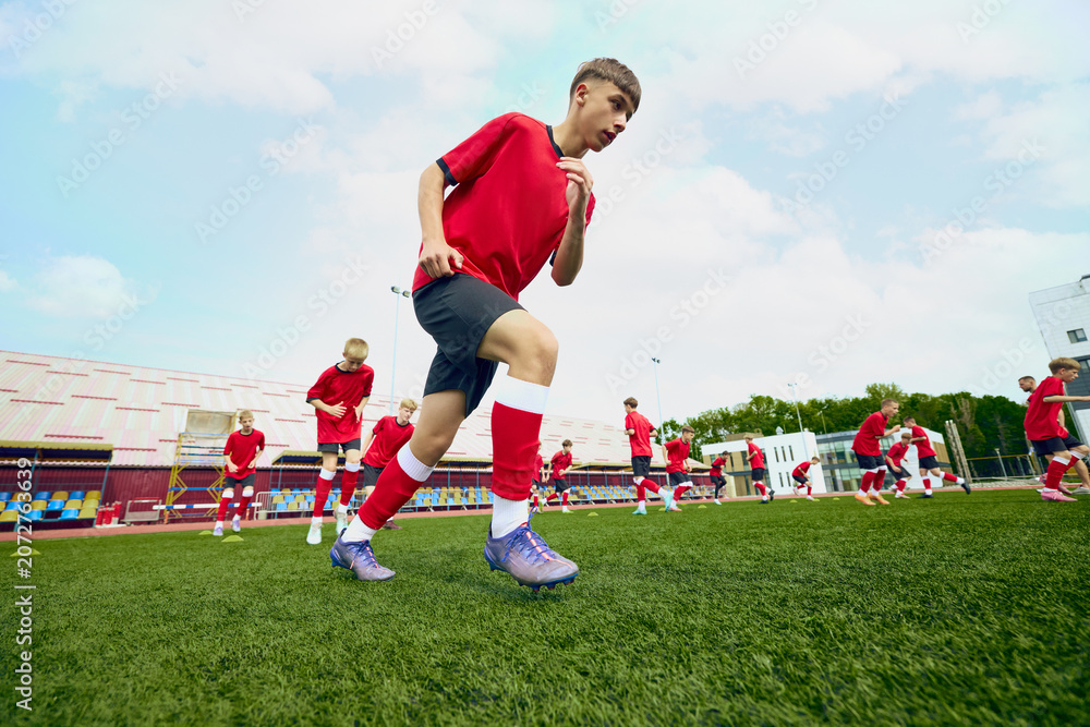 Obraz premium Youth soccer team running drills on stadium field. Concept of football academy practice, speed and agility training, school sports programs and youth brand ads.