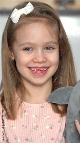 Portrait of little happy toothless girl with toy shark looks at camera and laughs. Baby milk teeth change. Health care. Vertical shot