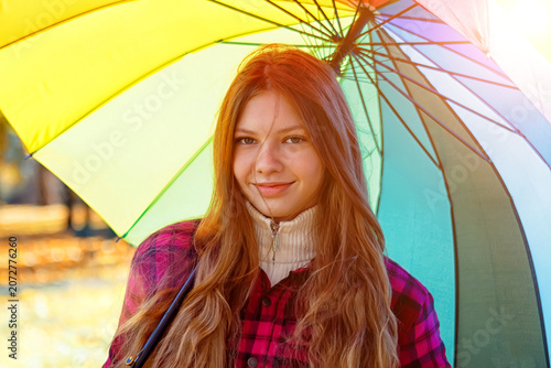 Young person holds a colorful umbrella in a park during sunny weather in autumn