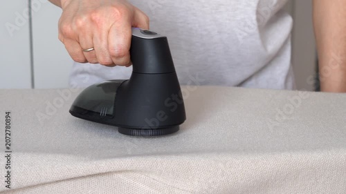Hand removes pills from knitted woolen clothing using fabric shaver. Textile pilling. Linting. Fabric lint, pilly, pellet, fluff.