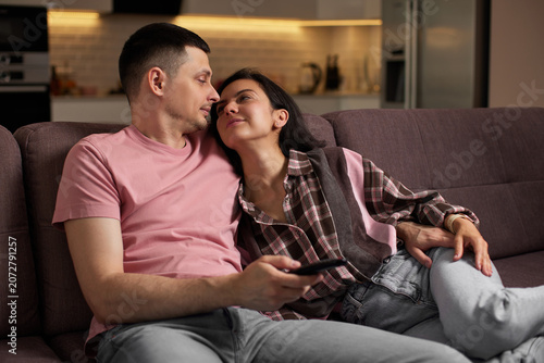 Young couple enjoying intimate moments at home, embracing on a couch while watching tv, finding comfort in their relationship