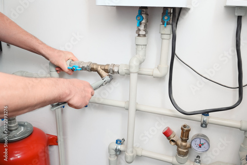 Fotografie Plumber tightening a pipe fitting with a wrench on a home heating system close u