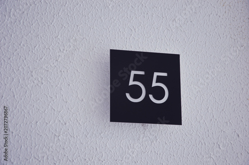 Minimalistic address plate with number 55 on a white wall.