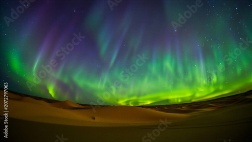 Vibrant green and purple aurora borealis display in the night sky over sand dunes transparent background