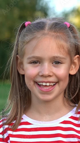 Portrait of happy girl looks at camera and laughs in summer park. Child outdoors. Vertical shot