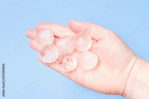 A woman's hand holding ice balls on a blue background close-up.
