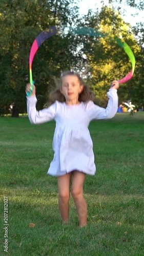 Happy girl jumps rope and laughs in summer park at sunset. Children play in nature. Kids leisure outdoors. Playground. Vertical shot