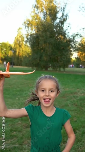 Happy girl runs and laughs with toy airplane in summer park. Children play in nature. Kids leisure outdoors. Playground. Vertical shot