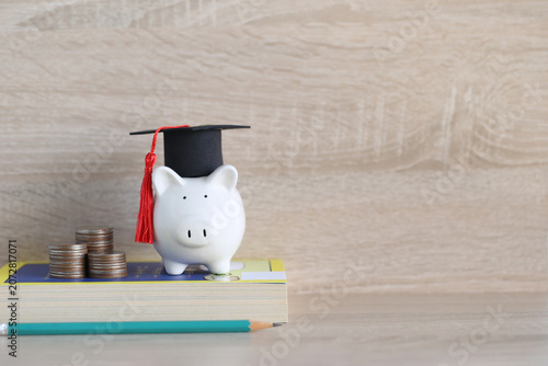 Graduation hat on blue piggy bank with stack of coins money on wooden background, Saving money for education concept