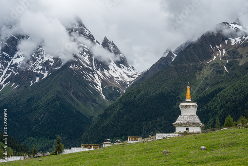 Photos The white stupa on a grassy slope beneath a snow-capped mountain shrouded in clo