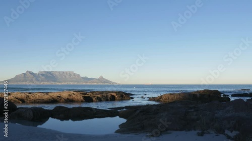 4K 25fps footage from Bloubergstrand showcasing the iconic Cape Town skyline with Table Mountain, Devil’s Peak and Lion’s Head across Table Bay under clear South African blue skies.