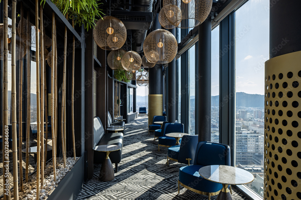 Obraz premium Stylish hotel rooftop bar with panoramic glass windows elegant blue velvet chairs and golden lamps