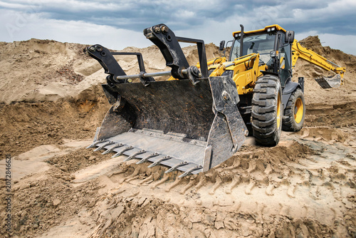 Universal excavator loader is performing work on a construction site. The machine is moving dirt and sand from one area to another during the day