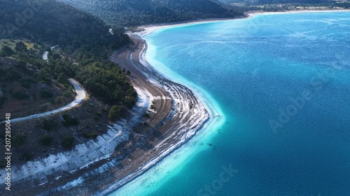A breathtaking drone view of Lake Salda, where its stunning turquoise waters meet the winding lakeside road and the green hills.