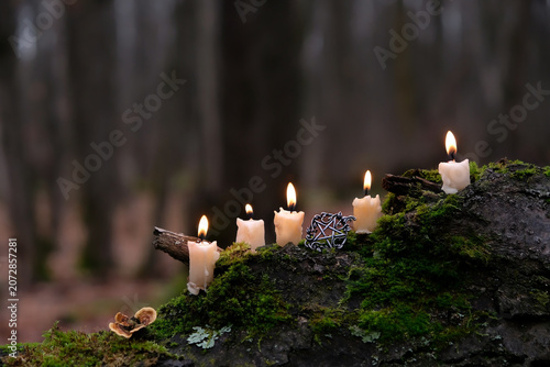 Bild auf Leinwand Burning wax candles and witch pentacle amulet close up on mossy tree trunk, natural dark forest background