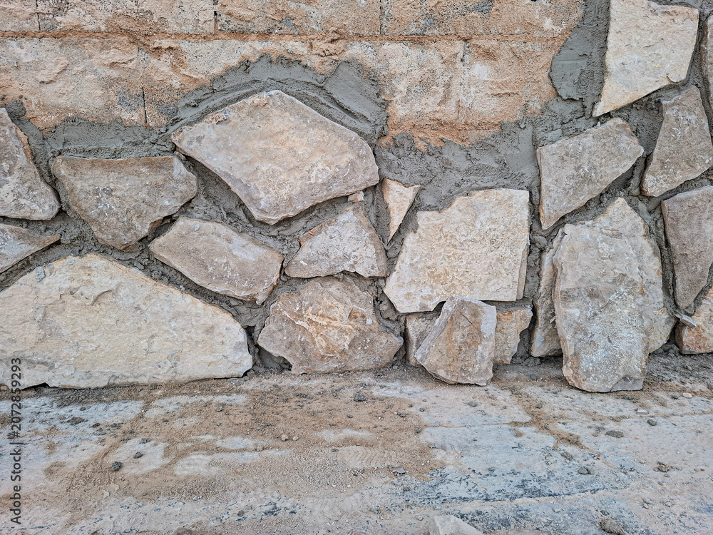 Fototapeta premium Building a rustic stone wall using beige limestone and grey cement mortar in a construction site