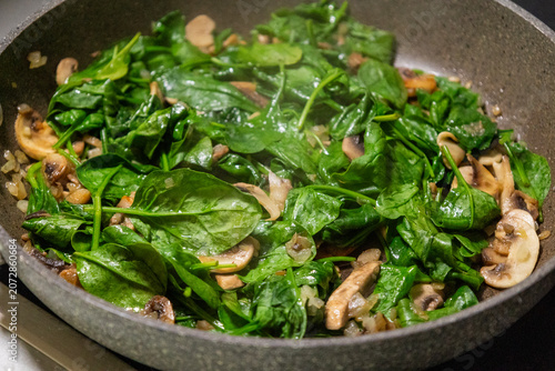 Tableau sur toile Macro close-up of sliced mushrooms and fresh green spinach leaves cooking and wi