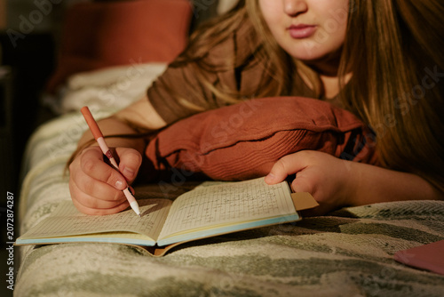 Schilderij op canvas Plus size girl writing in journal while lying on bed, reflecting on thoughts and daily routine