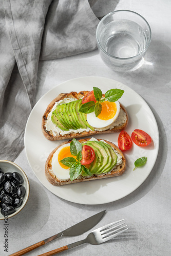 Two avocado toasts with egg, cream cheese, tomatoes, and basil on a concrete background